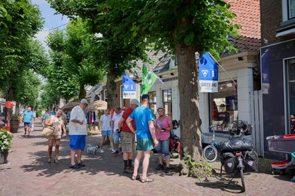 Meerdere zomers geklede mensen staan voor het VVV bezoekerscentrum in Langweer. Er hangen blauwe vlaggen uit.