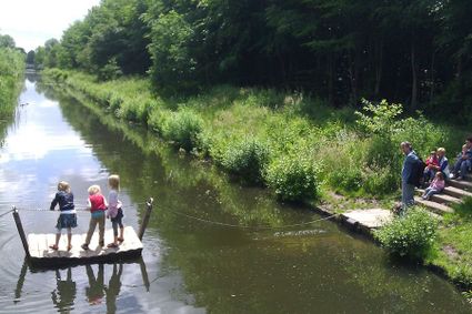 Kinderen trekken zich voort op een vlot op het water en aan de overkant staan andere kinderen te wachten voordat zij kunnen.