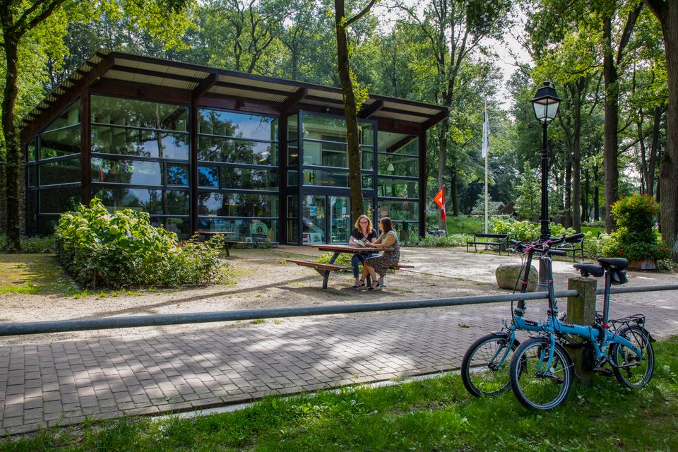 Twee mensen zitten op een picknickbank voor een informatiecentrum in de Drentse natuur.