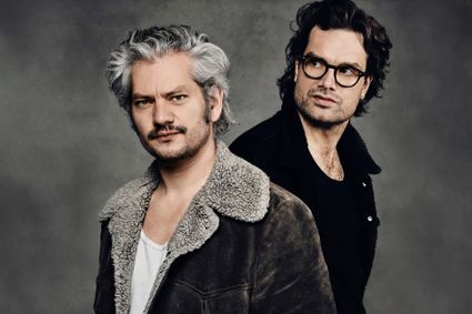 Theatervoorstelling van Maarten Heijmans en Xander Vrienten in Het Klooster Woerden, Groene Hart, met een portret van beide artiesten tegen een grijze achtergrond.