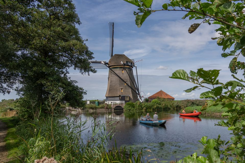 Twee mensen varen in een sloep langs de Heimolen in Aarlanderveen, omringd door groen en water in het Groene Hart van Holland.