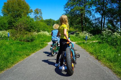 Fietsroute met kinderen in Woerden, Groene Hart. Kinderen fietsen over een groen fietspad door de natuur, omringd door bloemen en bomen, tijdens een gezinsuitje en recreatieve fietstocht in het Utrechtse buitengebied.