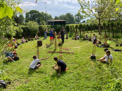 Workshop manden maken De Broedkorf in Oudewater, Groene Hart, groep kinderen en volwassenen vlechten met wilgentakken in het gras tijdens ambachtelijke buitenactiviteit met natuurlijke materialen.