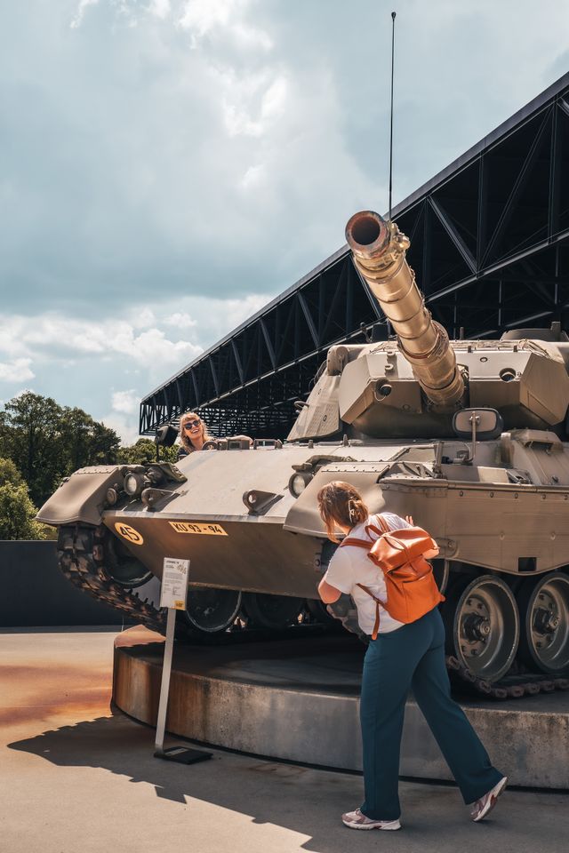Bezoekers bekijken een historische Leopard 1V tank bij het Nationaal Militair Museum in Soesterberg. De tank staat buiten voor het moderne museumgebouw.