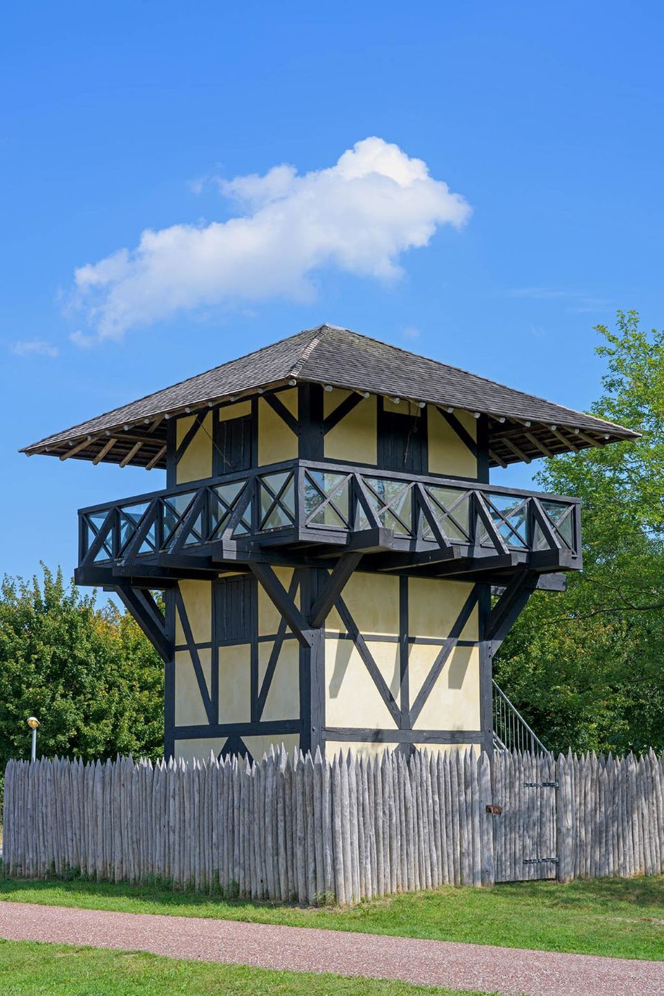 Een vierkante wachttoren van hout en leem, met een balustrade onder het dak en een hek om de toren.