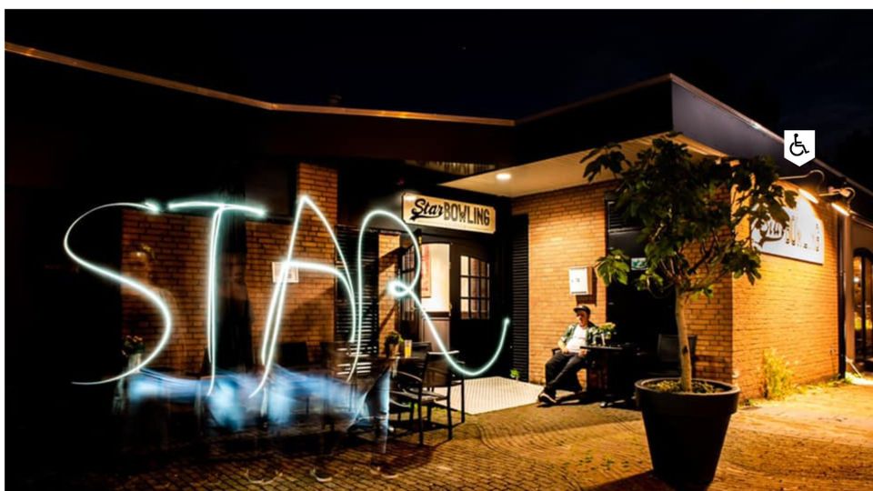 Uitgaanslocatie Star Bowling Woerden, provincie Utrecht, Groene Hart, nachtelijke sfeerfoto van het bowlingcentrum met verlichte entree, terras en lichtspoor voor de gevel.