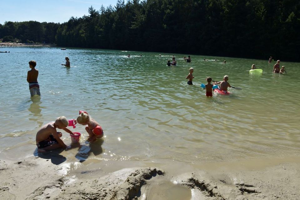 Kinder schwimmen und spielen im Badeweiher und im Sand.