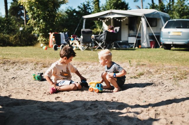 Zwei Jungen spielen mit Autos im Sand auf dem Campingplatz.