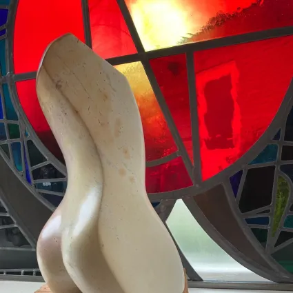 Beeldhouwwerk in de vorm van een witte torso tegen een glas in loodraam met rood als hoofdkleur