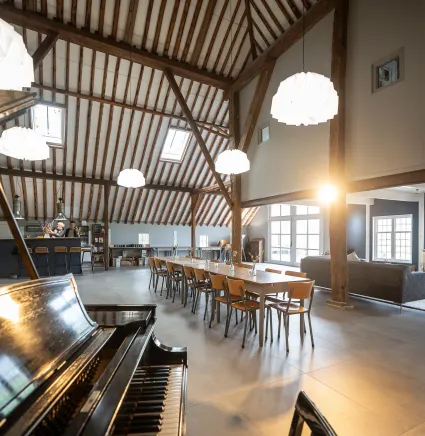 Groepsaccommodatie Nynke's Pleats in Piaam van de binnenkant met een piano op de voorgrond en een lange tafel met 15 stoelen.
