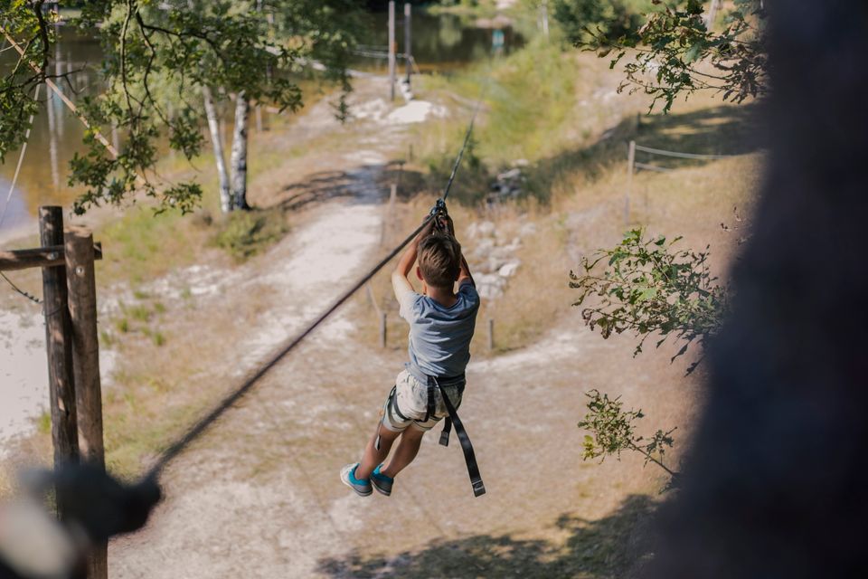 Junge fährt in einem Kletterpark eine Seilrutsche hinunter.