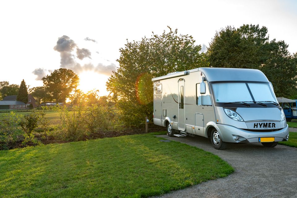 Een camper op een camper standplaats met een grasveld en op de achtergrond de ondergaande zon.