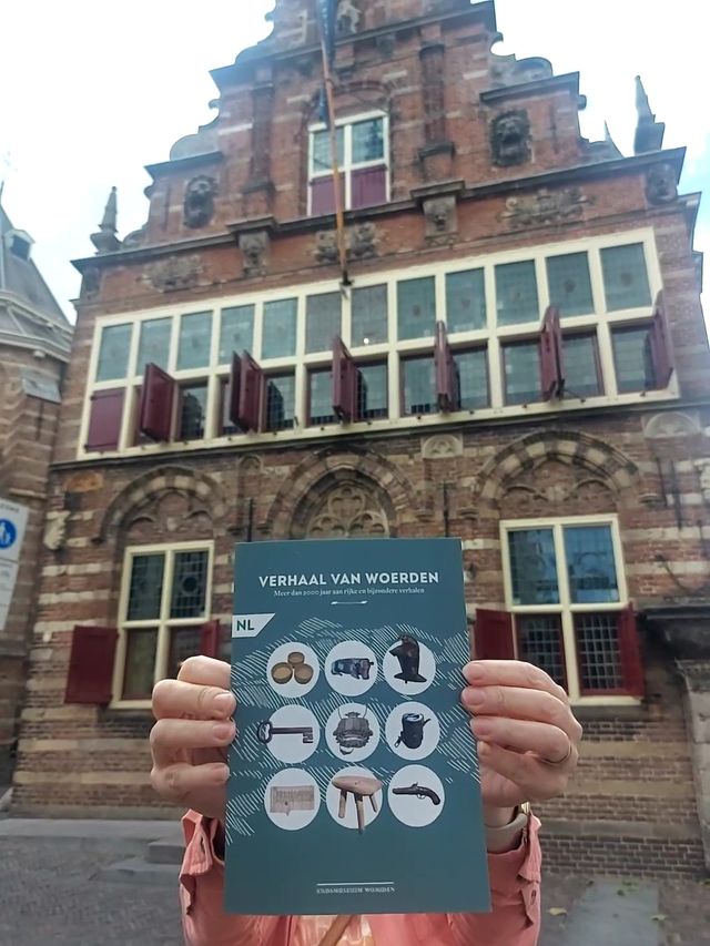 Tentoonstelling ‘Verhaal van Woerden’ bij Stadsmuseum Woerden, Groene Hart, met een bezoeker die de tentoonstellingsbrochure voor de historische gevel van het museum houdt.
