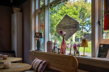 Koffiehuis Bij de Fortwachter met een sfeervolle zithoek, houten tafeltjes, bloemen, kleurrijke decoratie en grote ramen met uitzicht op de groene omgeving.