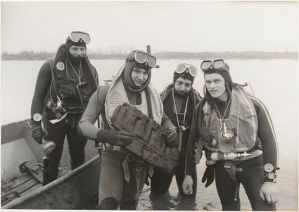 Foto uit de Tielse Courant met daarop vier leden van de Amsterdamse duikvereniging Manta poseren in november 1979 met een zojuist opgedoken plank, mogelijk van een platbodem.