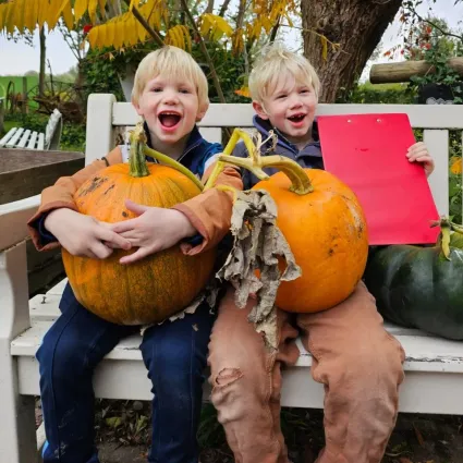 Twee lachende kinderen op een wit bankje met een oranje, ronde pompoen in handen