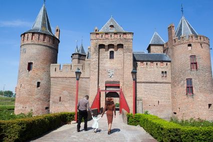 Twee volwassenen lopen met kindje tussen hen in de brug naar het Muiderslot op
