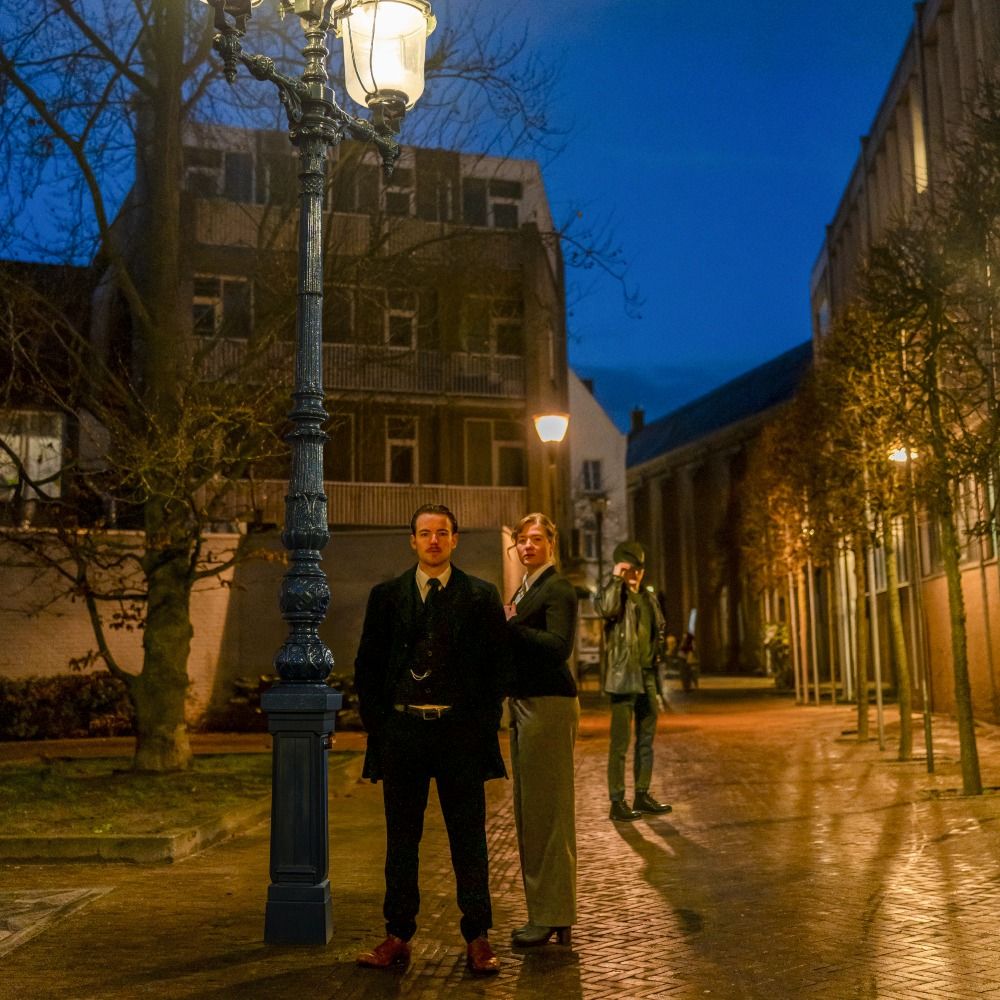 Foto van een duister straatje met 3 personen in het licht van een  lantaarnpaal.