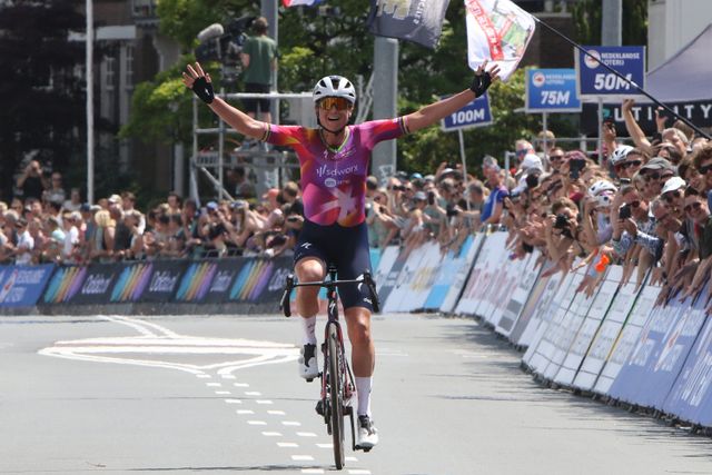 Wielrenster die over de finish fietst met juichend publiek ernaast