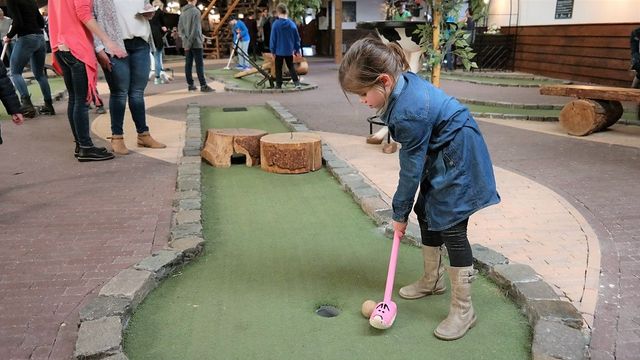 Kind speelt indoor mini-boerengolf bij Boerderij De Weistaar in Maarsbergen. De foto laat een speelse en kindvriendelijke activiteit op de boerderij zien.