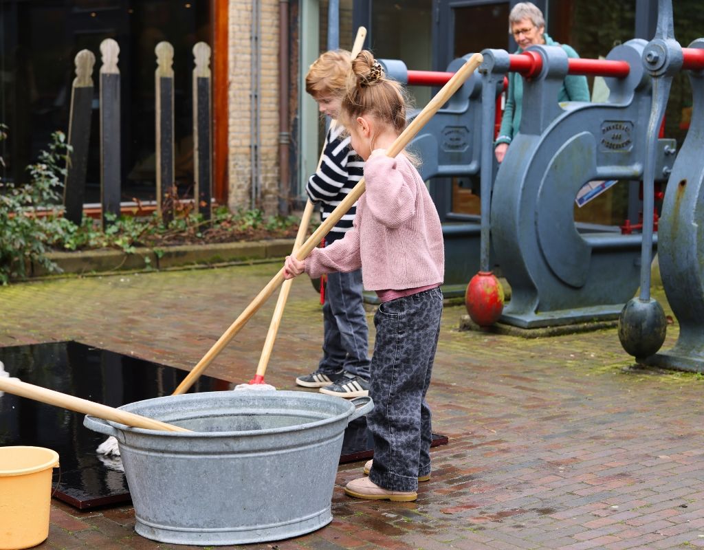 Jongetje en meisje met zwabber en teil met water in de tuin van het Fries Scheepvaart Museum