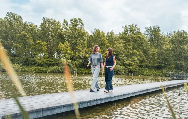 Twee vriendinnen lopen over een smalle pier over het water