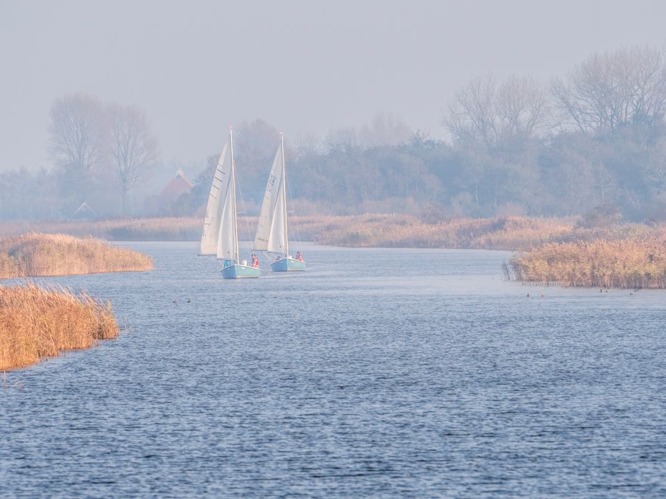 Twee zeilboten varen in winter in water bij woudsend.