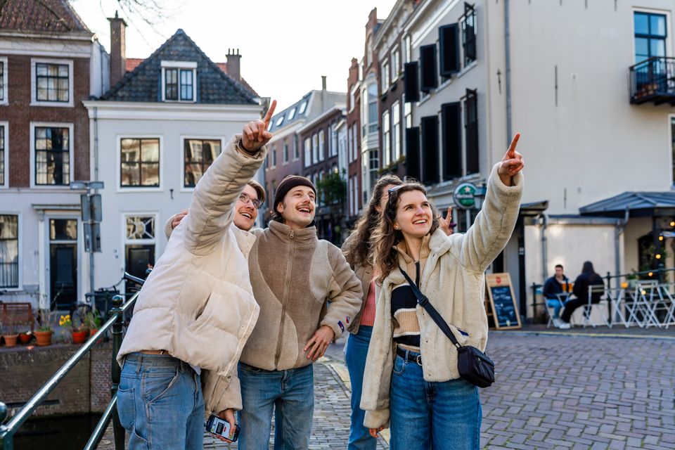 Groep vrienden ontdekt Oudewater tijdens een city escape en wijst enthousiast naar historische gebouwen in de sfeervolle binnenstad.