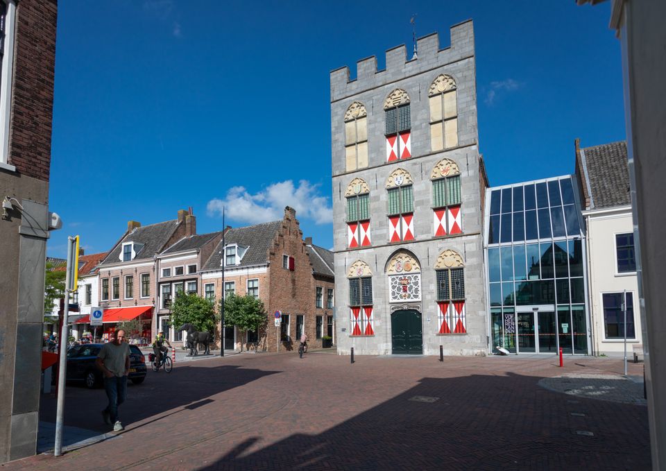 Het stadhuis van Vianen, een groot grijs gebouw, met rood witte luikjes voor de ramen.