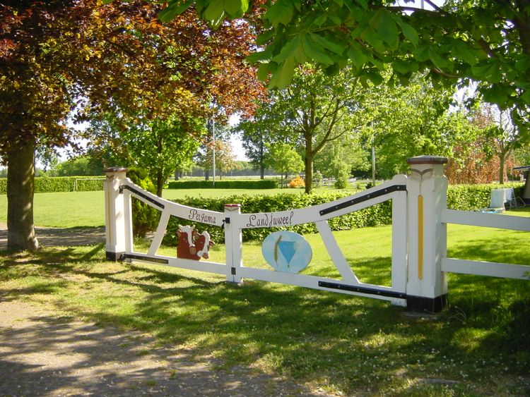 Zonnige foto van een grasveld met bomen en op de voorgrond een wit, houten sierhek.
