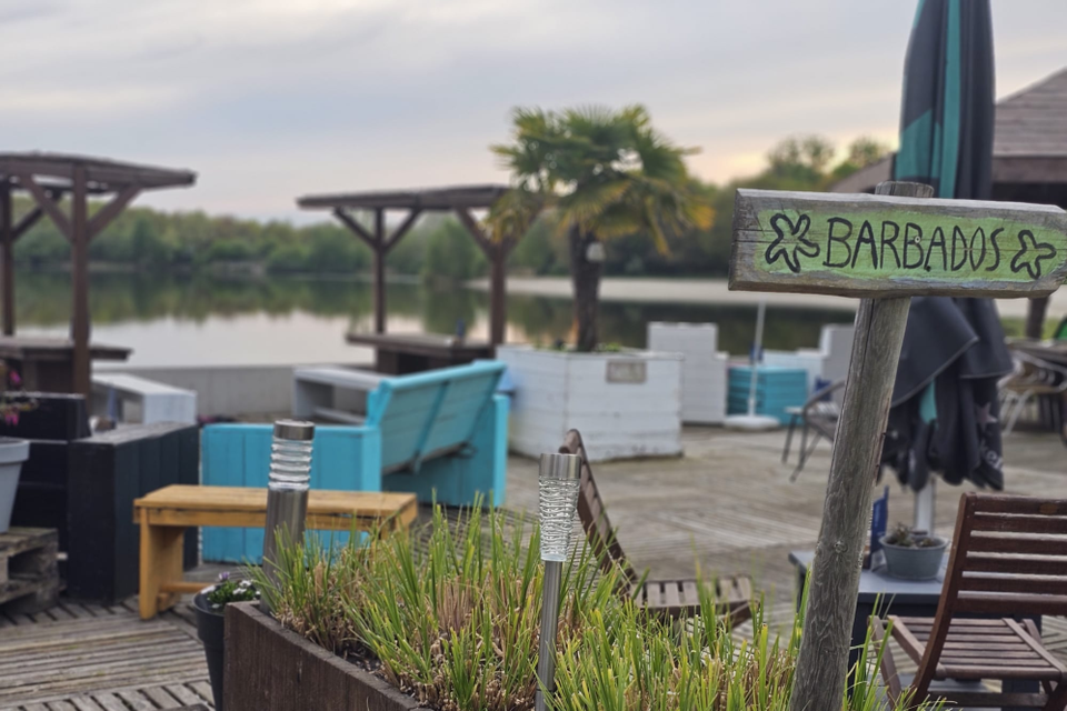 Een terras met houten banken aan het strand bij een zwemplas.