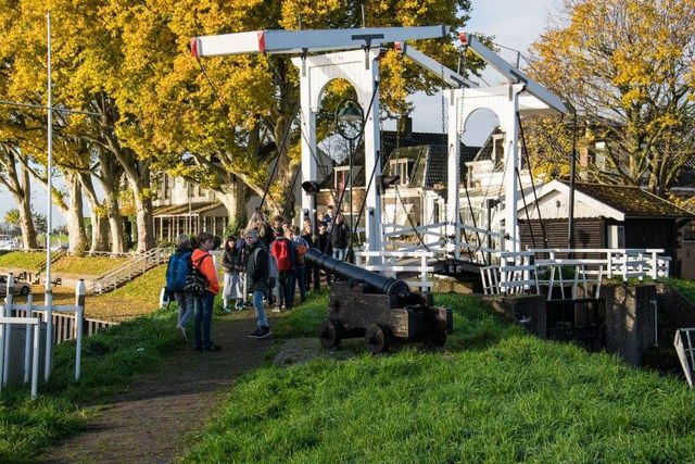 Een groep kinderen wandelen voorbij het kanon van Schoonhoven, over het witte bruggetje heen.