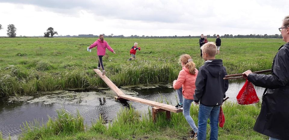 Kinderen die over houten planken over de sloot lopen