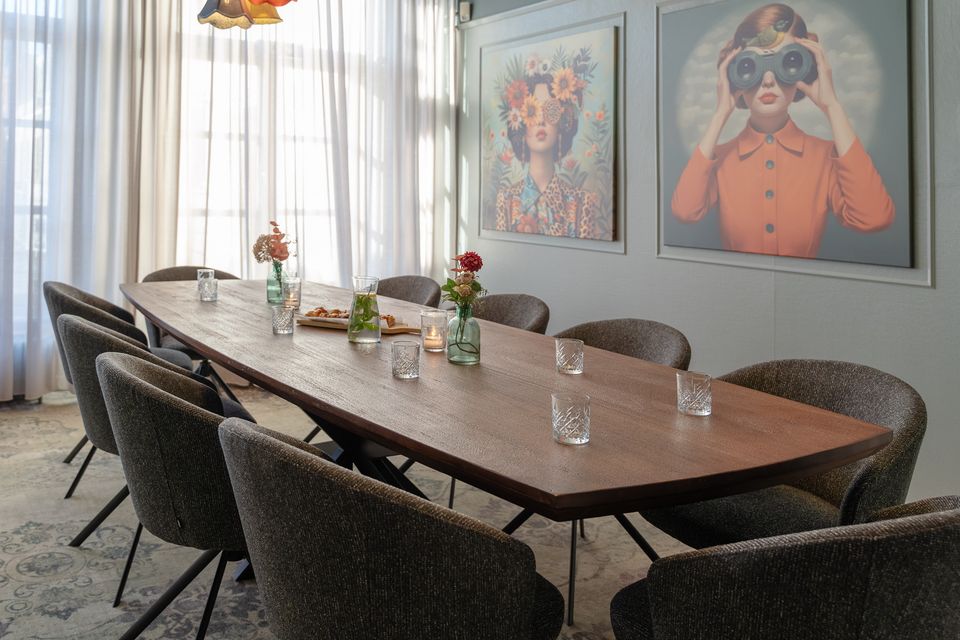 Vergaderlocatie Plein 7 in Woerden, Groene Hart, sfeervolle vergaderzaal voor zakelijke bijeenkomsten met lange houten tafel, comfortabele stoelen, bloemen en kleurrijke wanddecoratie.