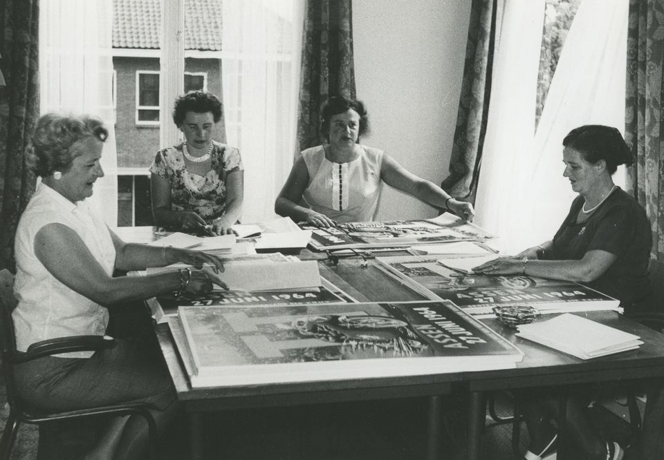 Voorafgaande aan de TT van 1964 wordt de verspreiding van o.a. posters voorbereid op het TT-bureau aan de Torenlaan te Assen. Rechts zit mevrouw Weggemans. De overige personen zijn niet bekend.