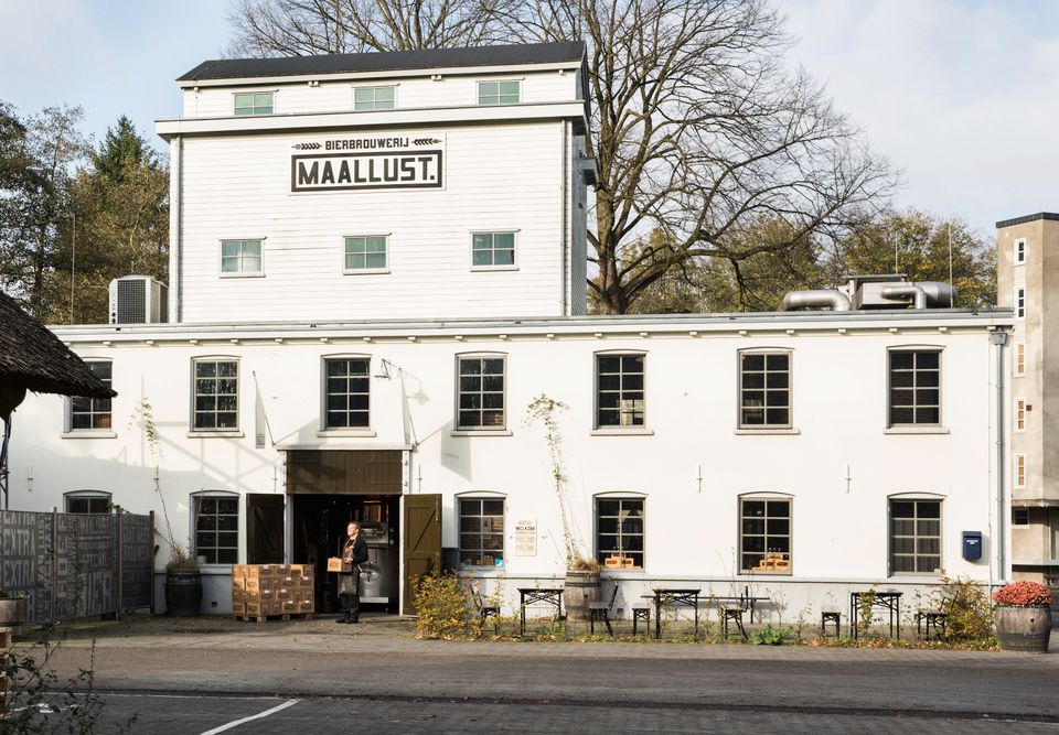 Gebouw van Maallust in Veenhuizen. In de deuropening een man die een kistje met bier draagt.