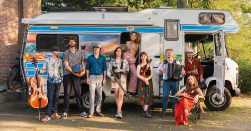 Een band die voor een camper staat met muziekinstrumenten