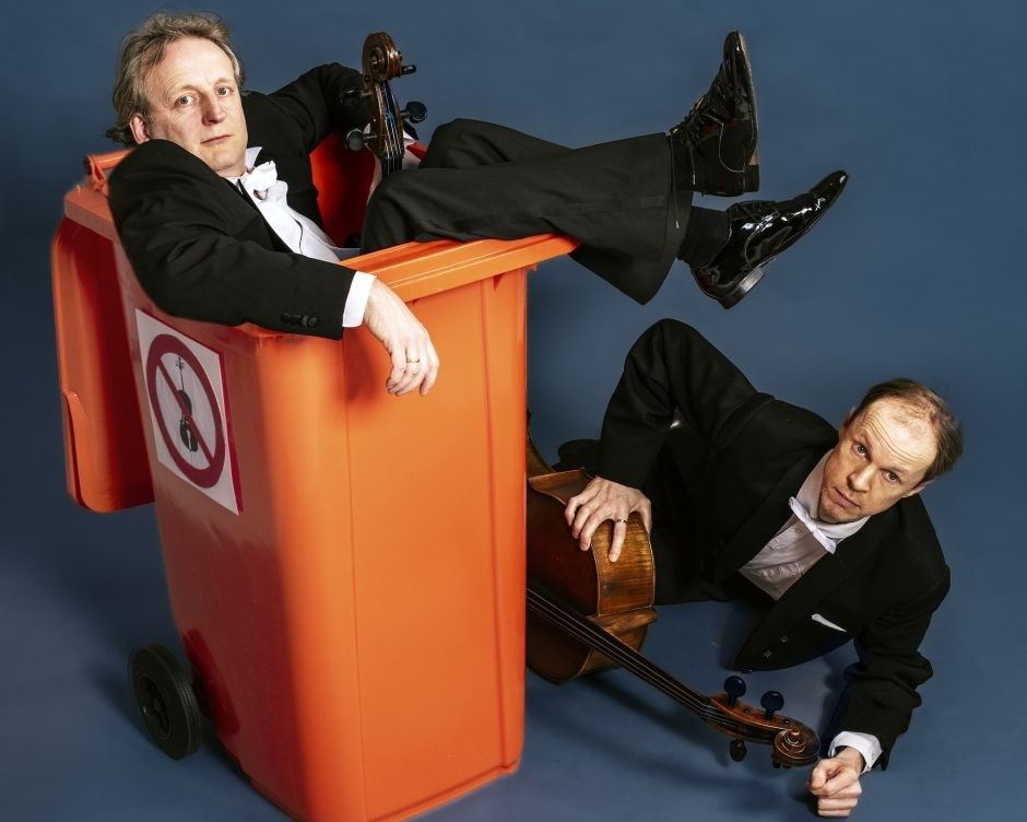Het Cello duo zit bij een oranje afval kliko