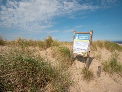 Foto van de strand met een bord en op het bord staat informatie over de schonen strand.