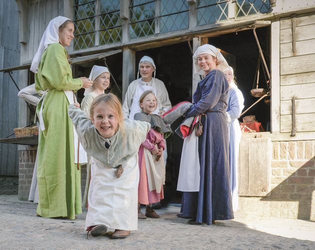 Kinderen in middeleeuwse kleding spelen en lachen bij een historische boerderij in Archeon, een educatief openluchtmuseum in het Groene Hart.