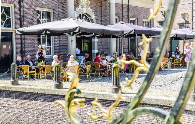 Het terras van Kasteel Groeneveld zit vol met mensen die genieten van het zonnetje en een lekker drankje