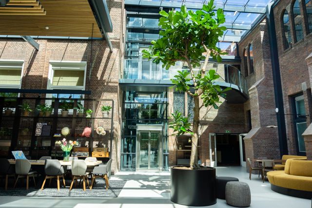 Licht en modern restaurant KonneKt van Hotel Kontakt der Kontinenten in Soesterberg, ingericht in een voormalige kloosteromgeving. De hoge glazen overkapping, bakstenen muren en grote boom zorgen voor een sfeervolle en groene uitstraling.