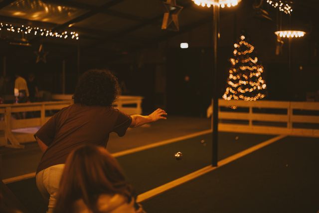 Sfeervolle indoor jeu-de-boulesbaan bij Boerderij De Boerinn, met speler die een bal werpt en warme kerstverlichting op de achtergrond – gezellige winteractiviteit in het Groene Hart.