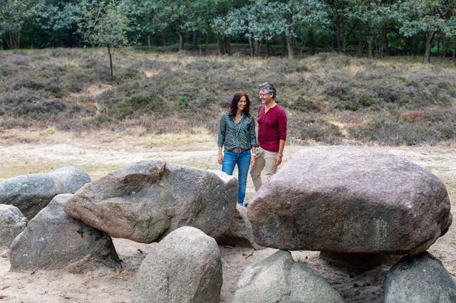 Man en vrouw staan lachend naar een hunebed te kijken.