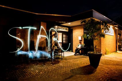 Uitgaanslocatie Star Bowling Woerden, provincie Utrecht, Groene Hart, nachtelijke sfeerfoto van het bowlingcentrum met verlichte entree, terras en lichtspoor voor de gevel.