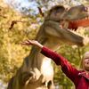 Meisje gooit met herfstbladeren met op de achtergrond een dino