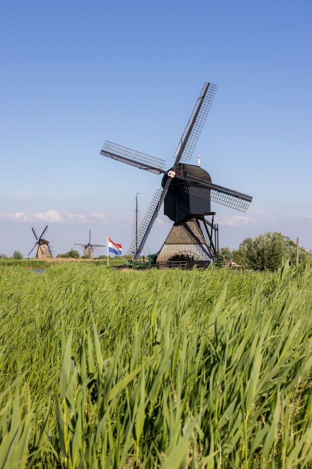 Een molen met op de achtergrond nog twee molens, en een Nederlandse vlag.