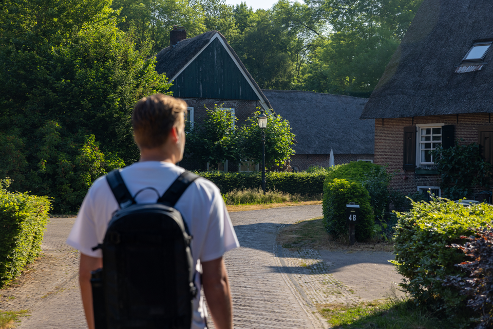 Een man met rugzak wandelt door de straten van een authentiek Drents dorpje met Nedersaksische boerderijen.
