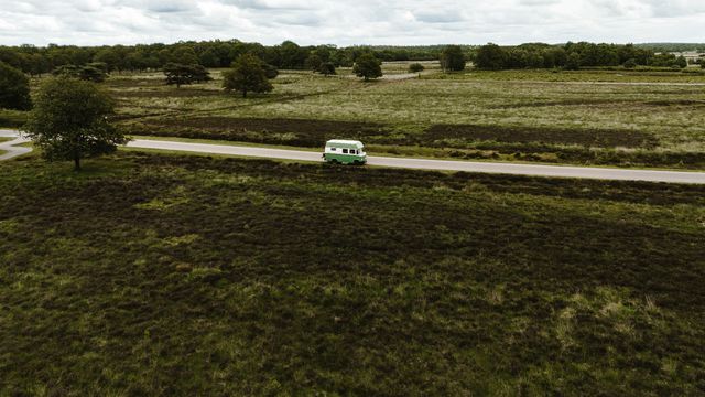 Het groen witte busje van Tralaluna Casita on Wheels rijdt langs uitgestrekte heidevelden in de Drentse natuur.