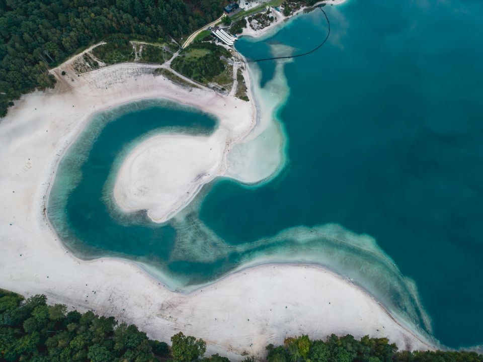 Dronefoto van een blauwe waterplas aan zand- en bosgebied in Nederland